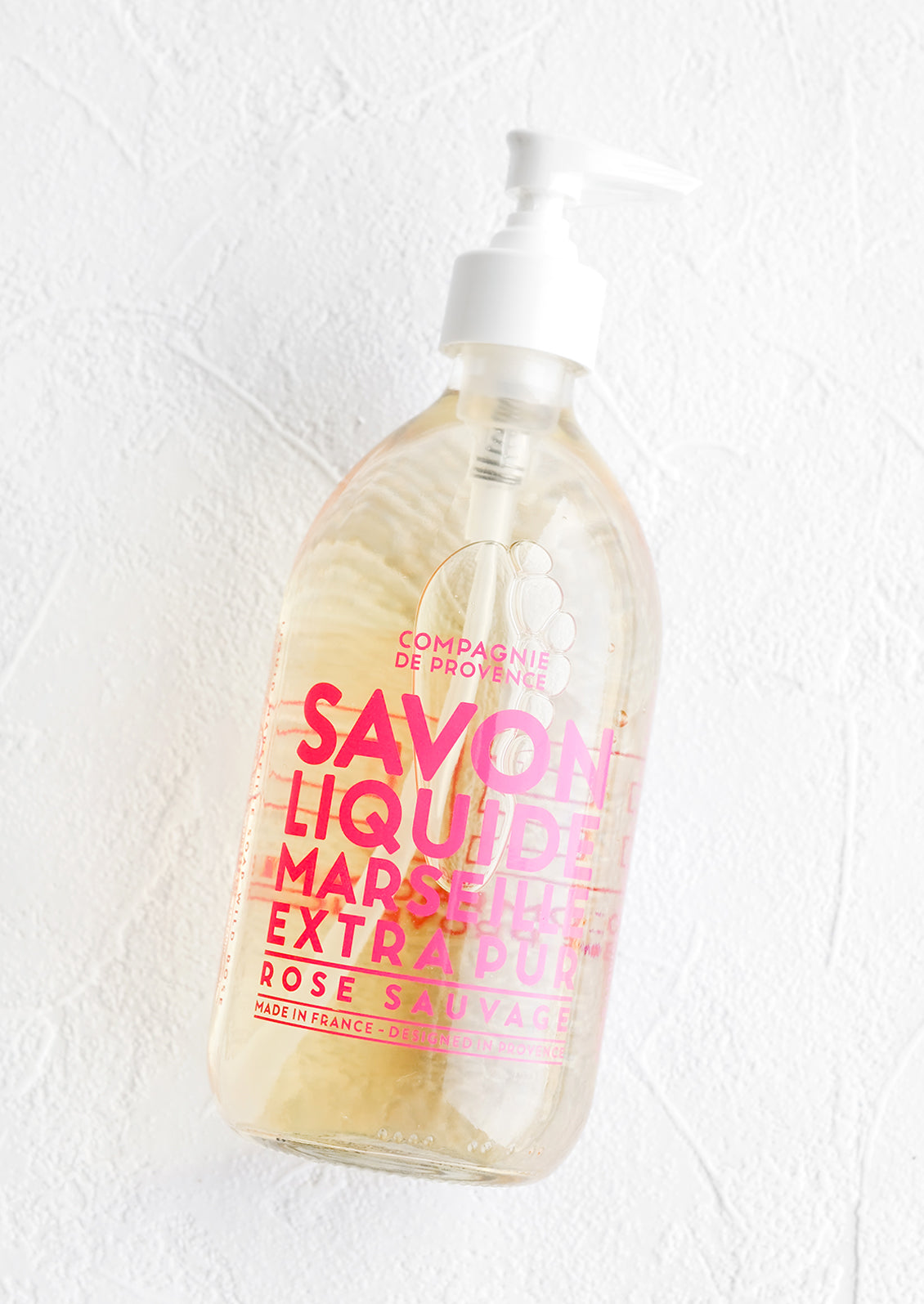 A clear glass soap bottle with bold pink text printed on bottle