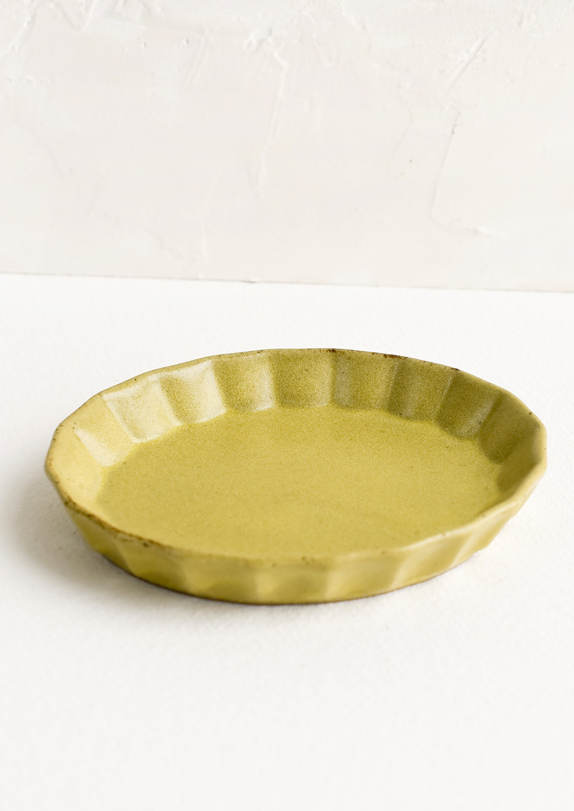 A small, oval shaped shallow dish with pleated edge in matte chartreuse glaze.