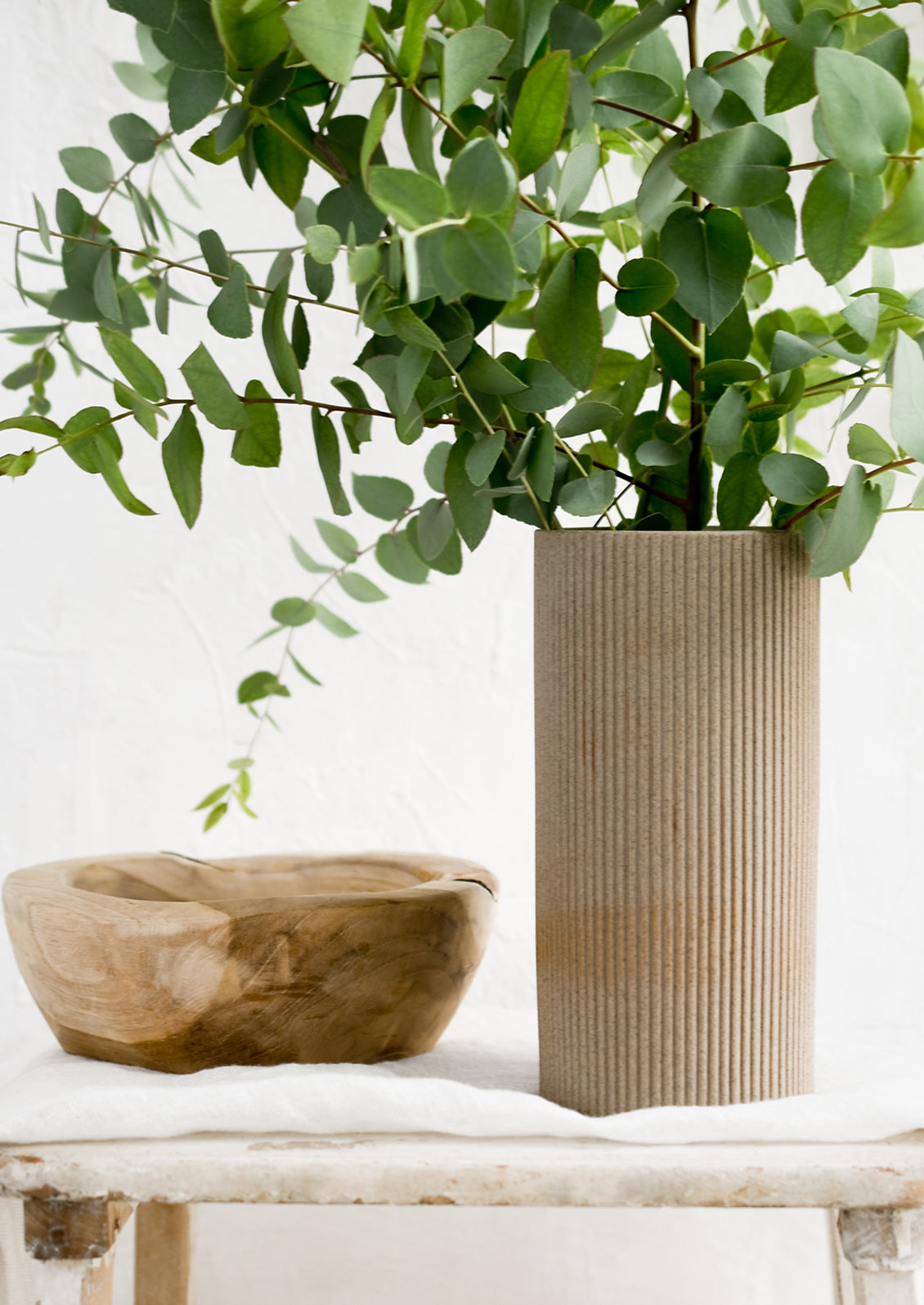 Eucalyptus in a sandy brown vase with wooden bowl.