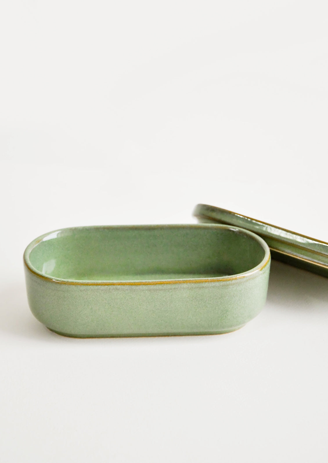 Oblong oval ceramic green Container with lid lying by its side.