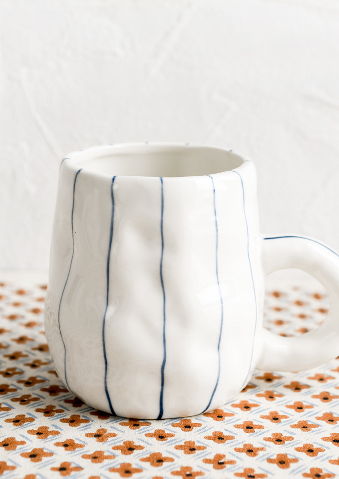 A pinched white mug with vertical thin blue stripes.