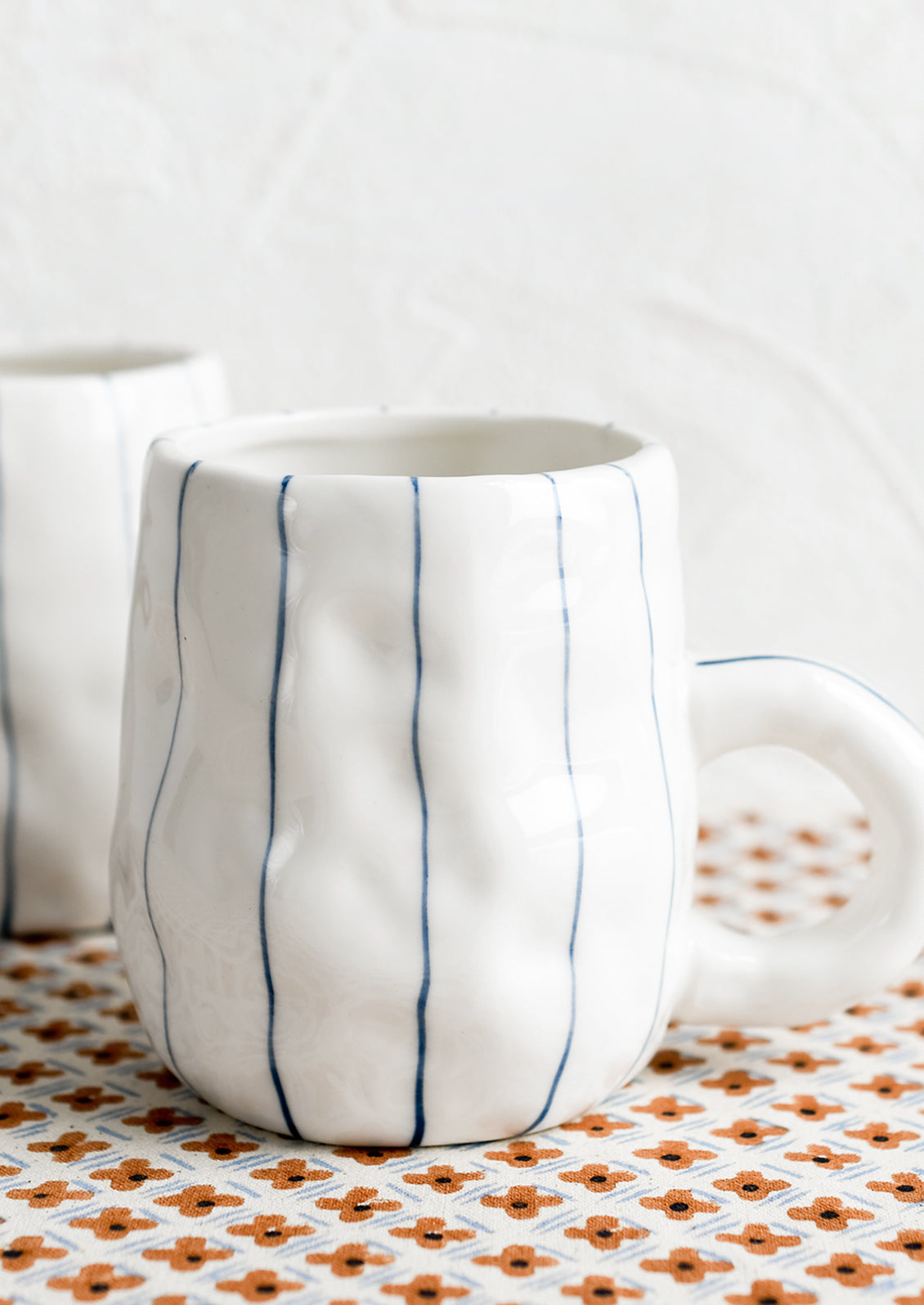 A pinched white mug with vertical thin blue stripes.