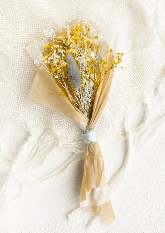 A small bouquet of dried yellow, white and light blue flowers wrapped in parchment paper