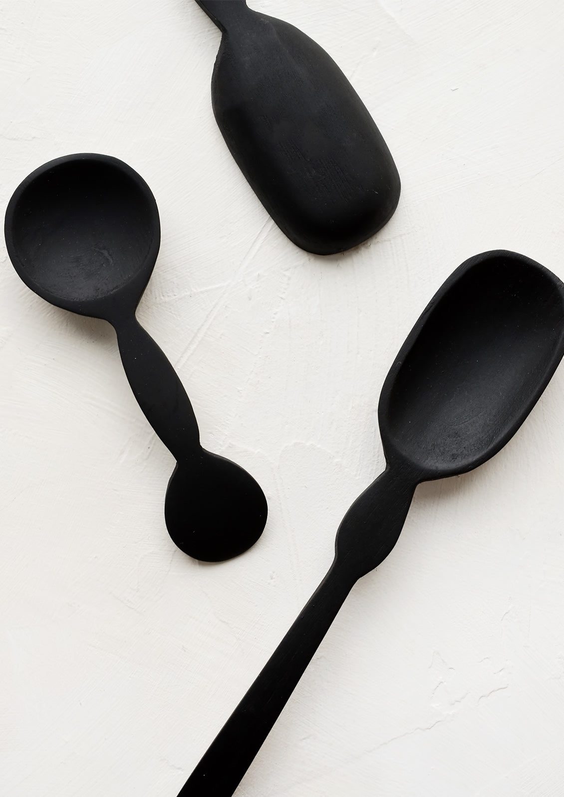 An assortment of carved black wooden spoons in a mix of shapes and sizes.