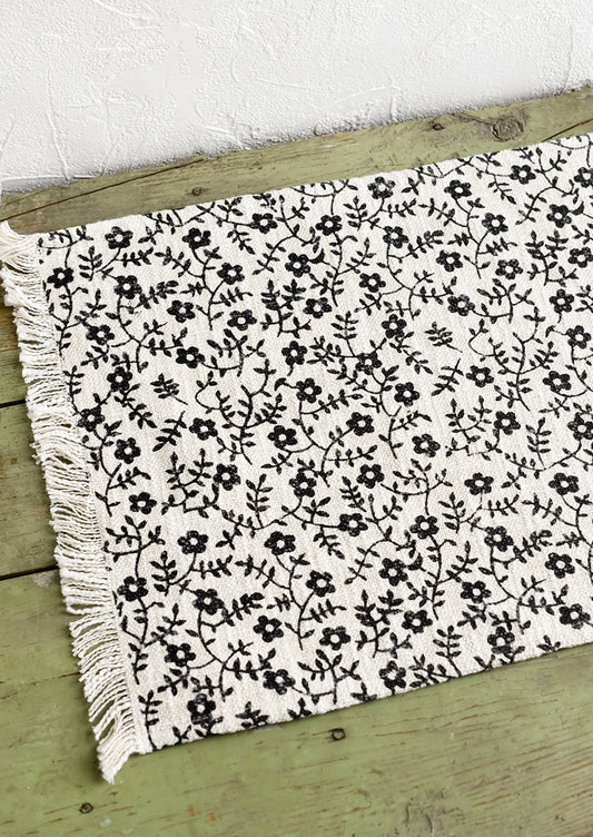 A black and white floral print placemat with fringe trim.