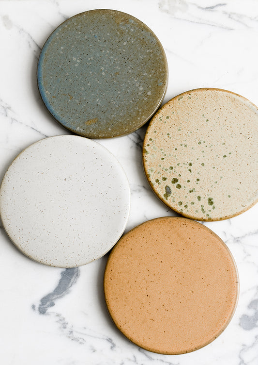 A set of four round ceramic coasters in earthy color mix.