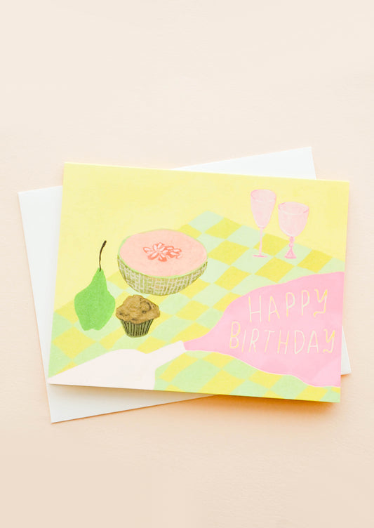 Greeting card with picnic setting, spilled wine puddle has letters reading "Happy Birthday"