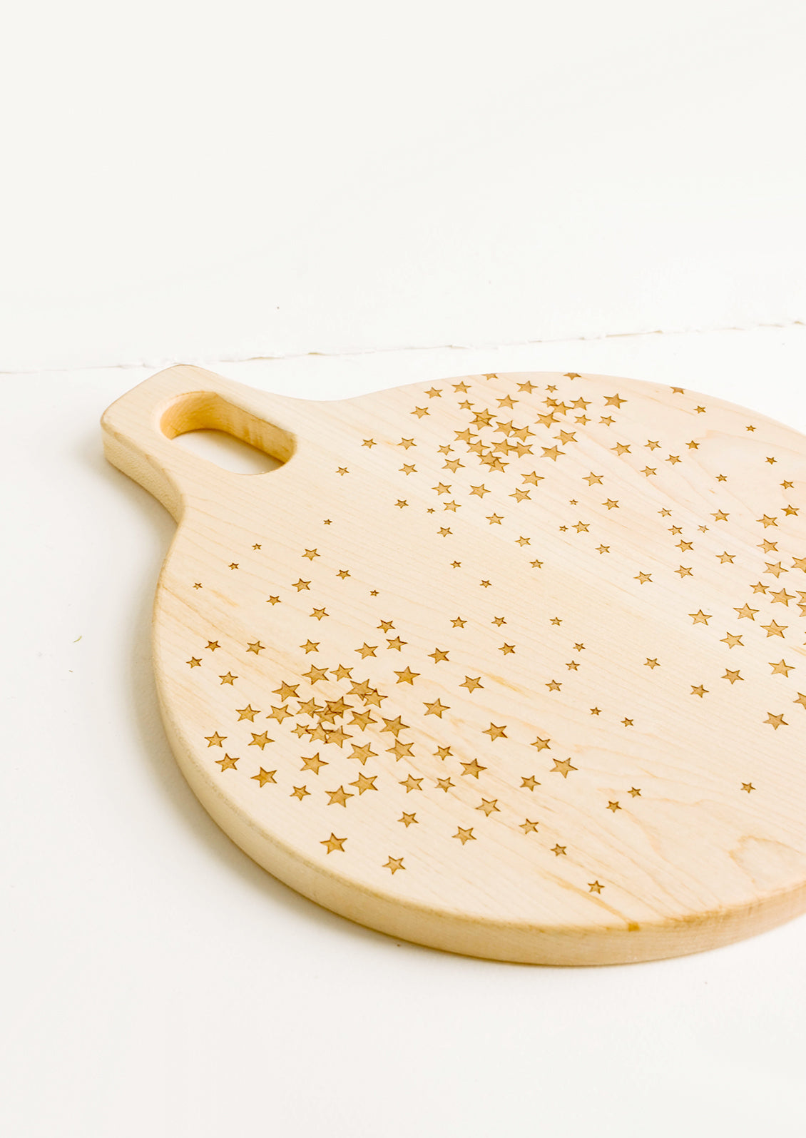 Round paddle-style cutting board in maple wood with scattered star pattern