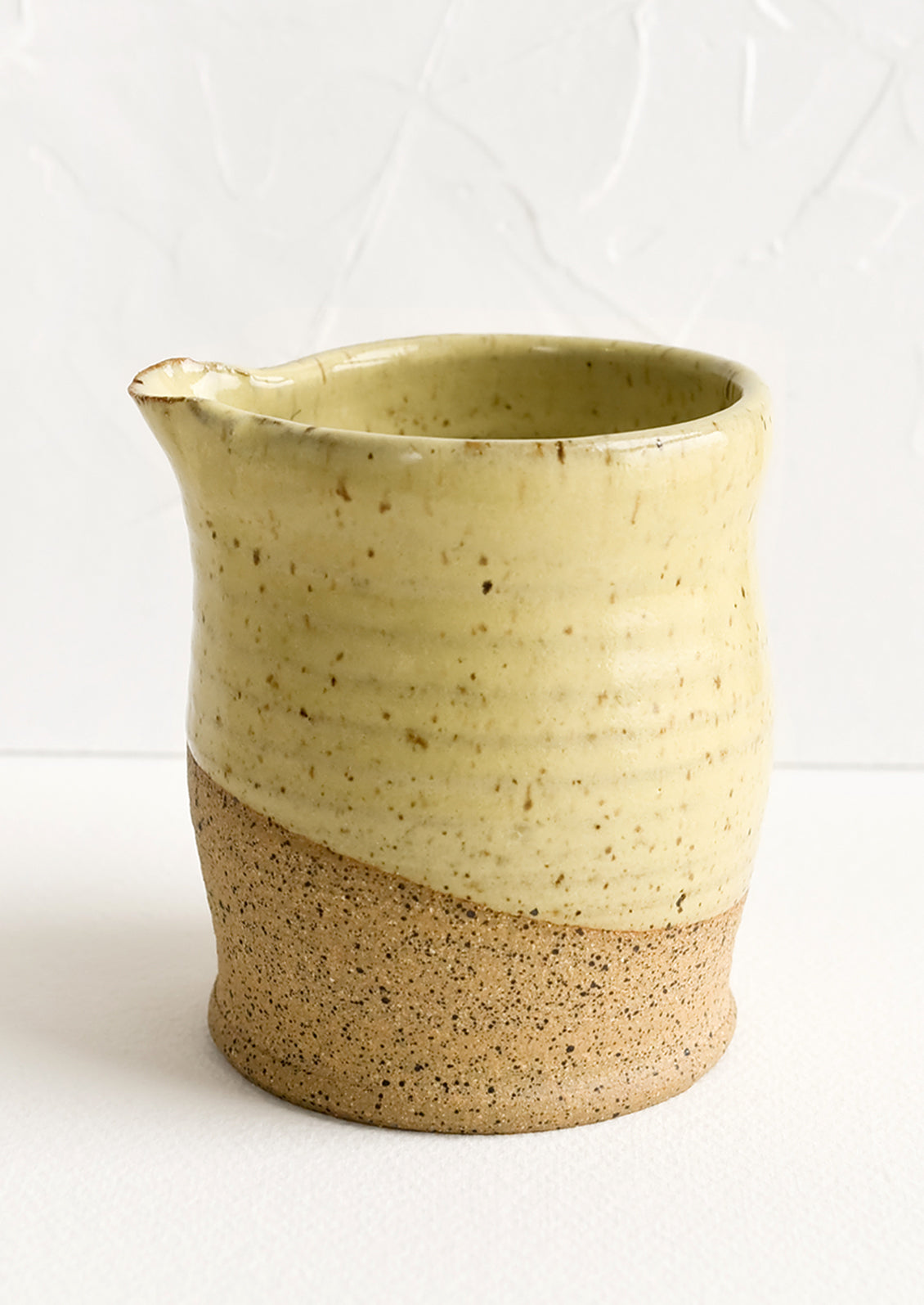 A small ceramic pitcher in dipped speckled yellow glaze.