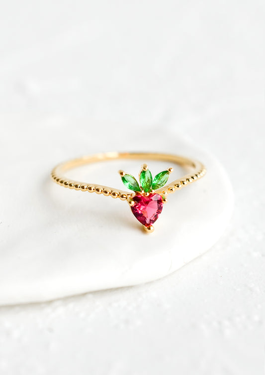 A gold ring with beaded texture and strawberry shaped crystal front.