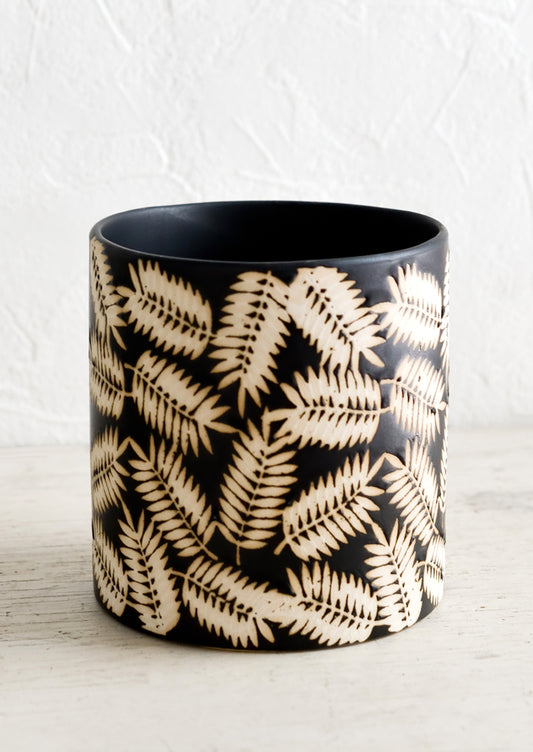 A round black ceramic planter with resist print of palm leaves.