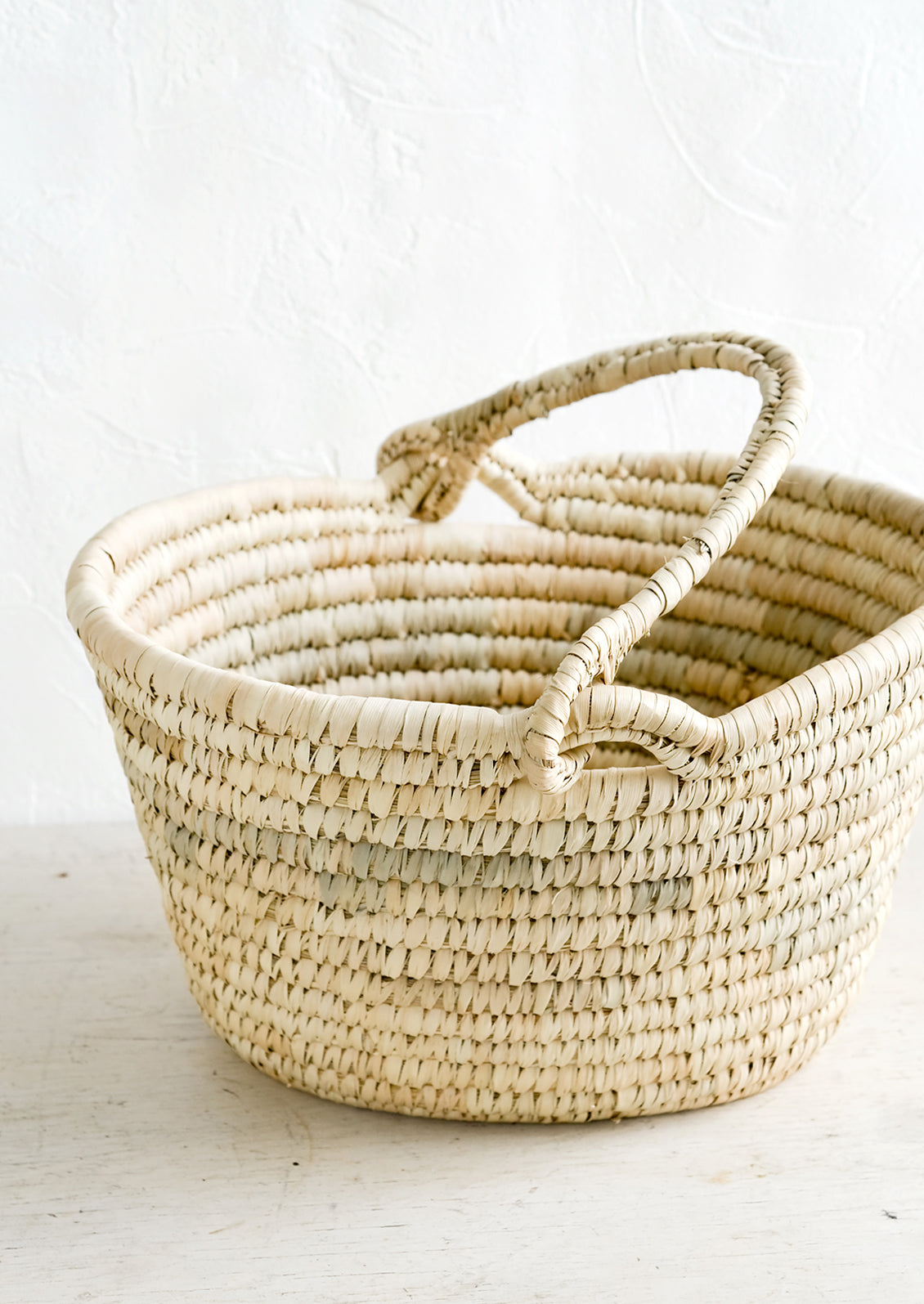 An oval shaped basket made from natural straw with a mobile top carrying handle.