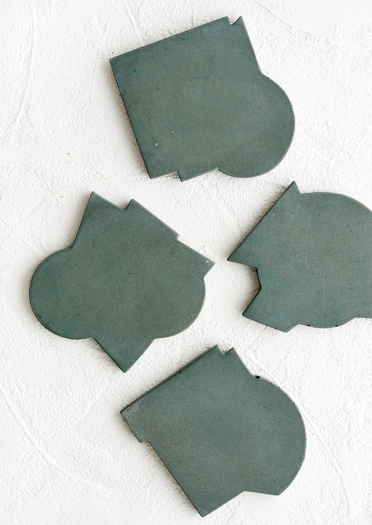 Four concrete coasters in petrol blue-green color with unique abstract shapes.