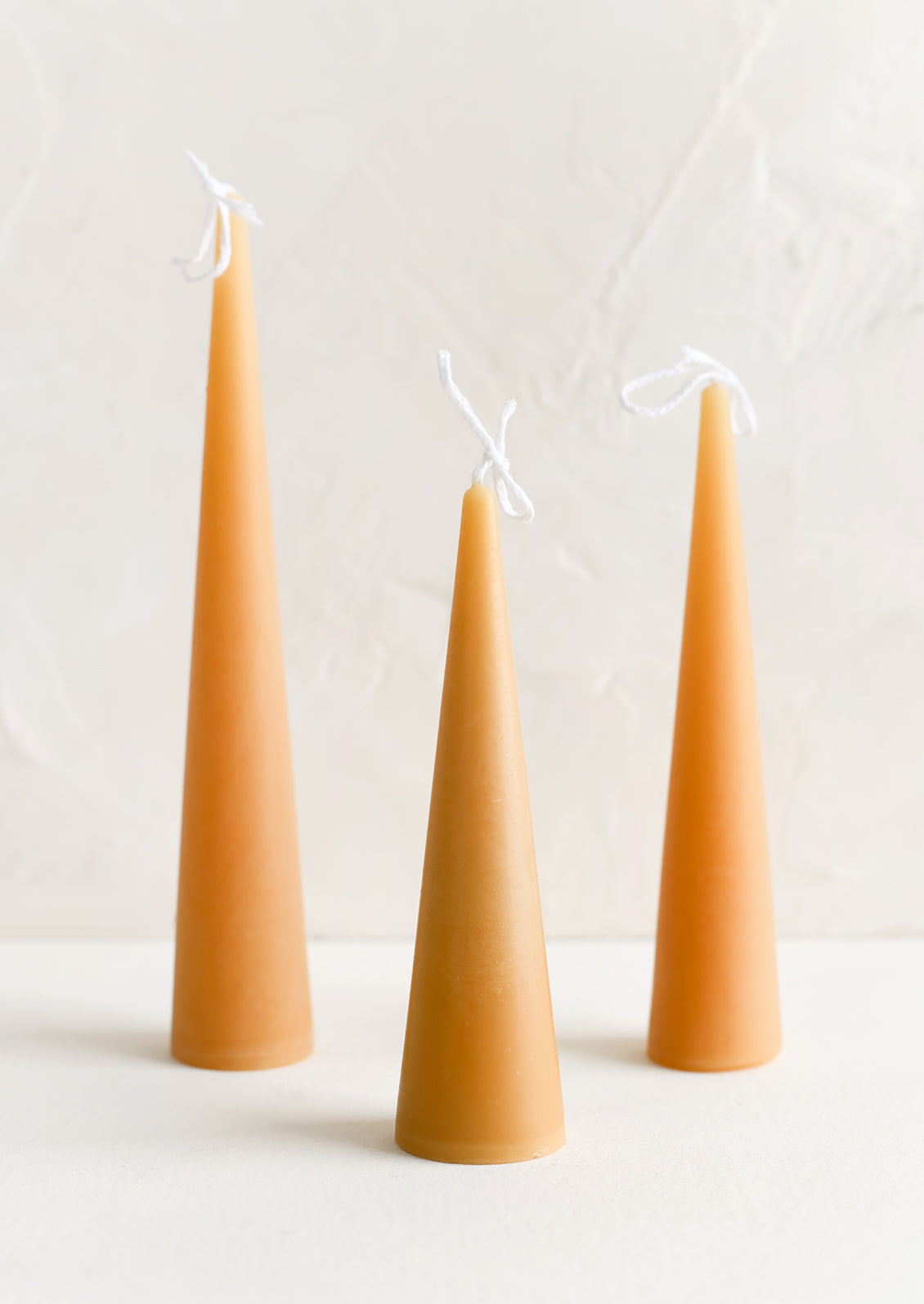 Three lit cone-shaped taper candles in warm sand.