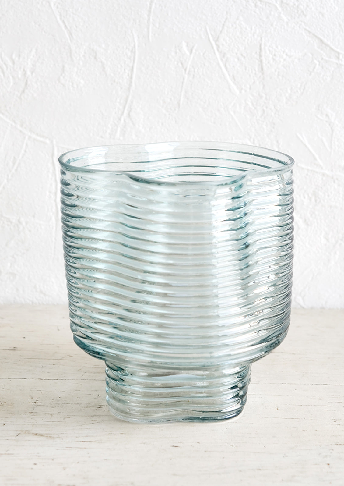 A curvy flower vase in light blue ribbed glass.