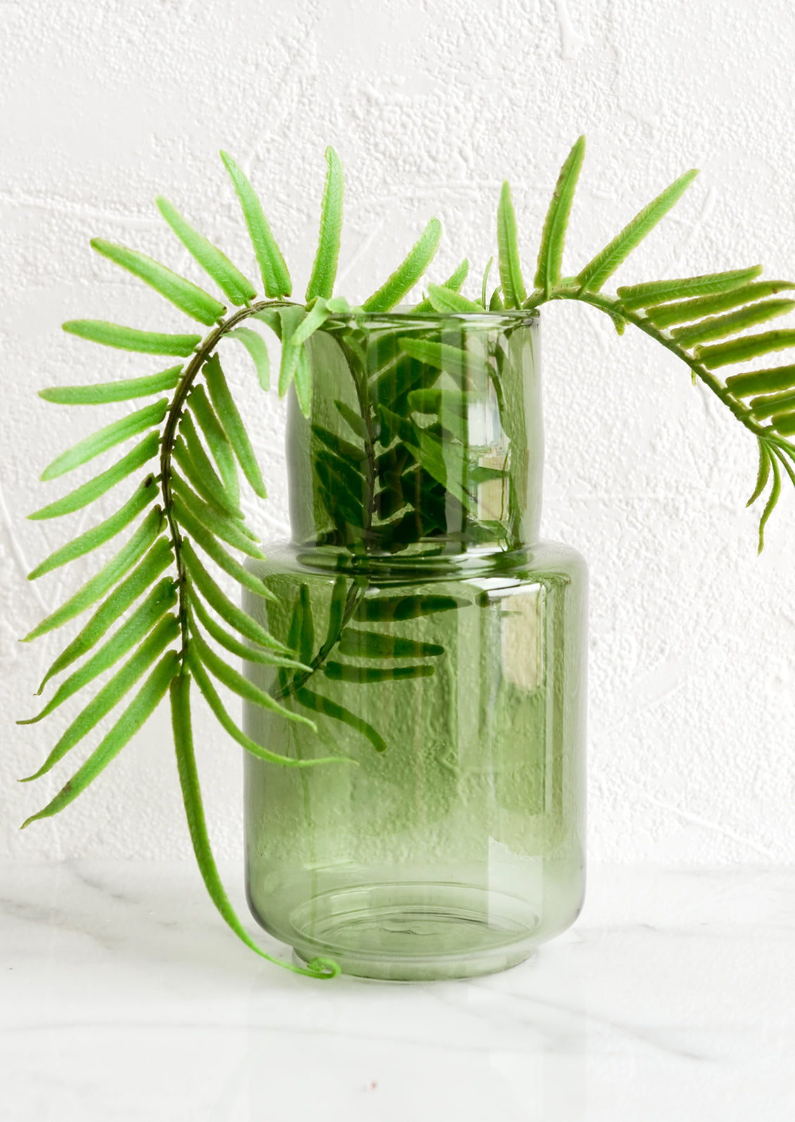 A green glass vase with fern.