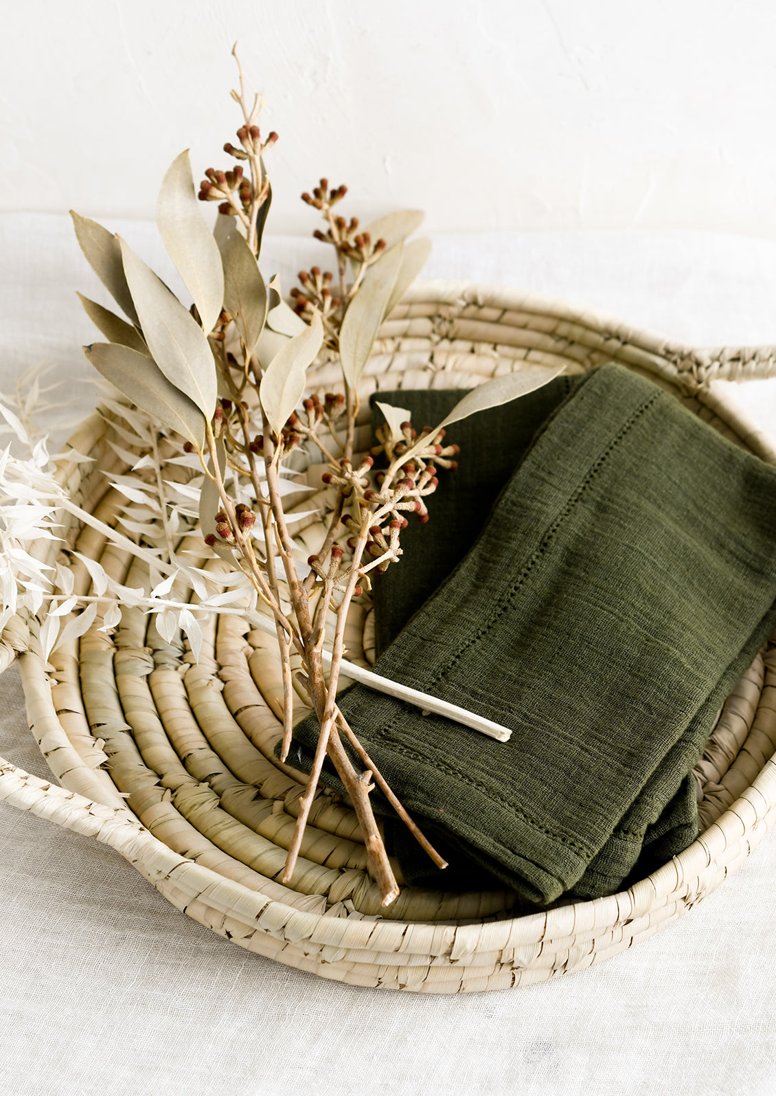 A round woven tray holding dried flowers and napkins.