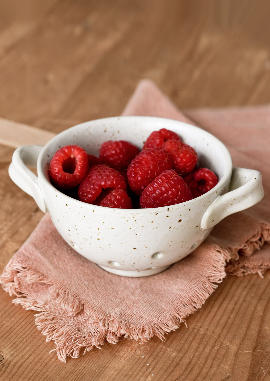 A small ceramic colander holding raspberries.