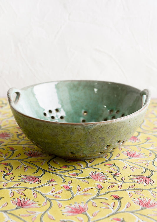 A large ceramic colander in mottled aqua glaze.