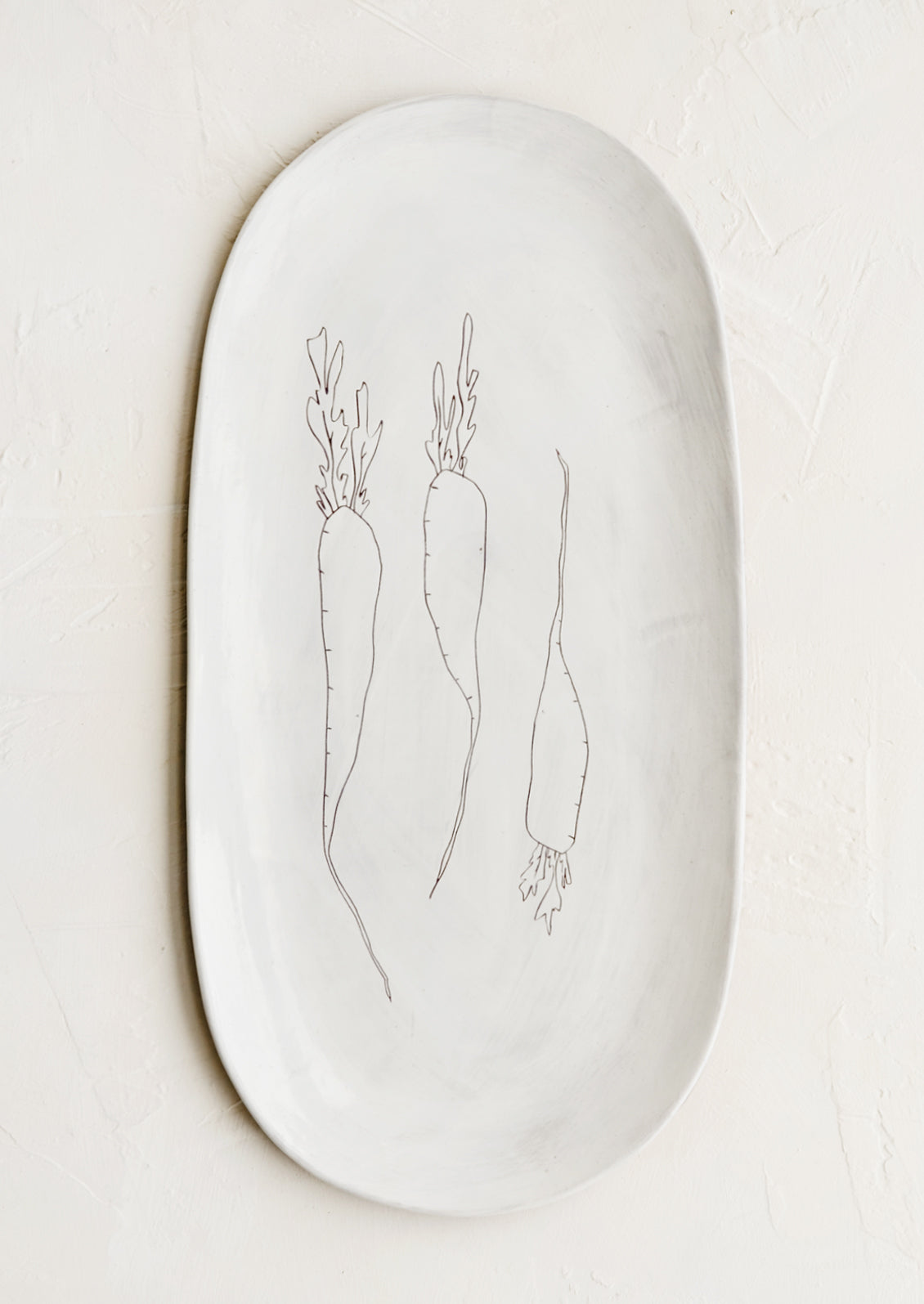 An oval shaped ceramic serving platter with hand drawn carrots illustration at center.