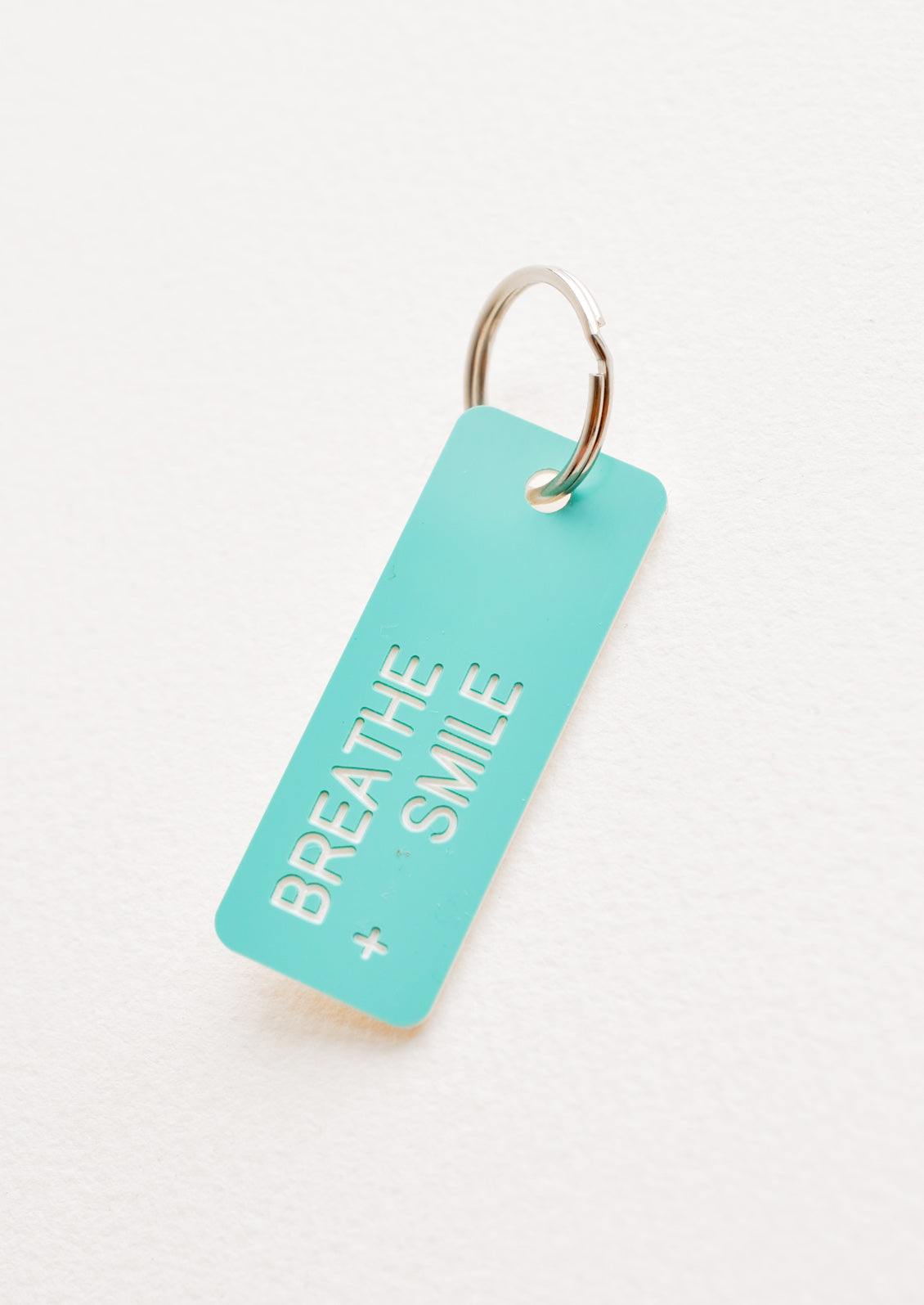 Small acrylic keychain, turquoise background with white words that says "BREATHE + SMILE"