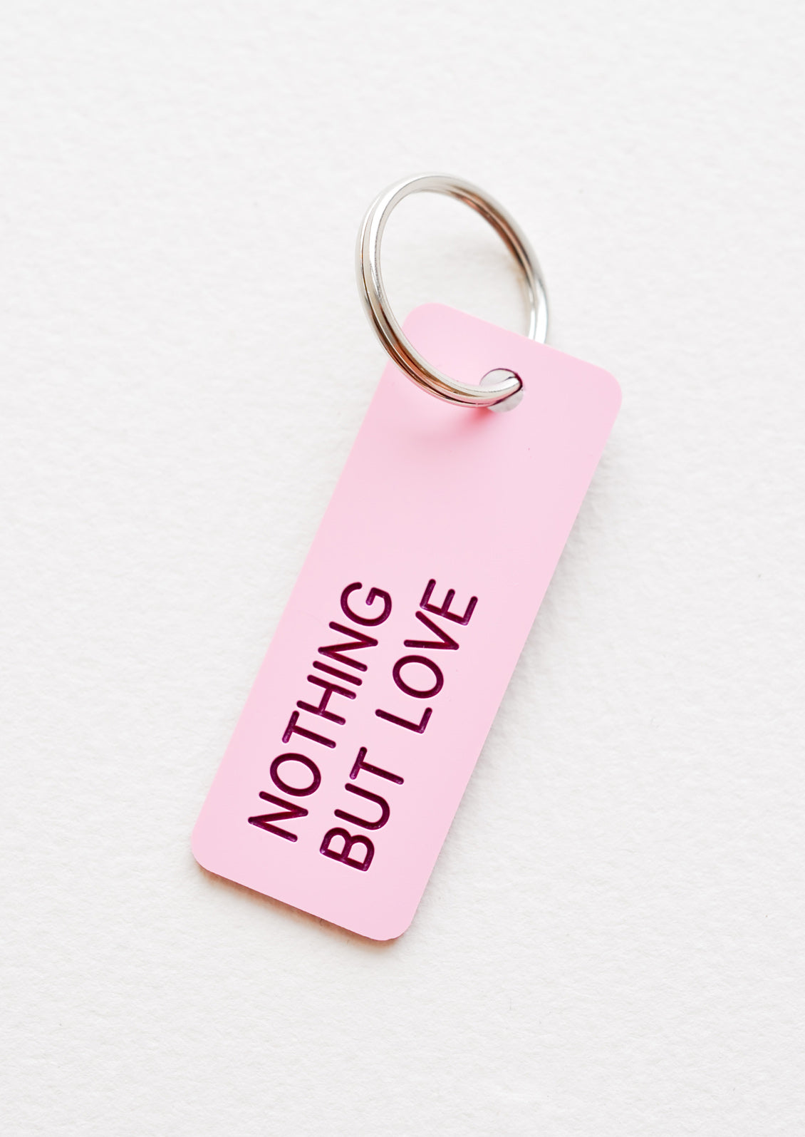 Small acrylic keychain, pink background with red words that says "NOTHING BUT LOVE"