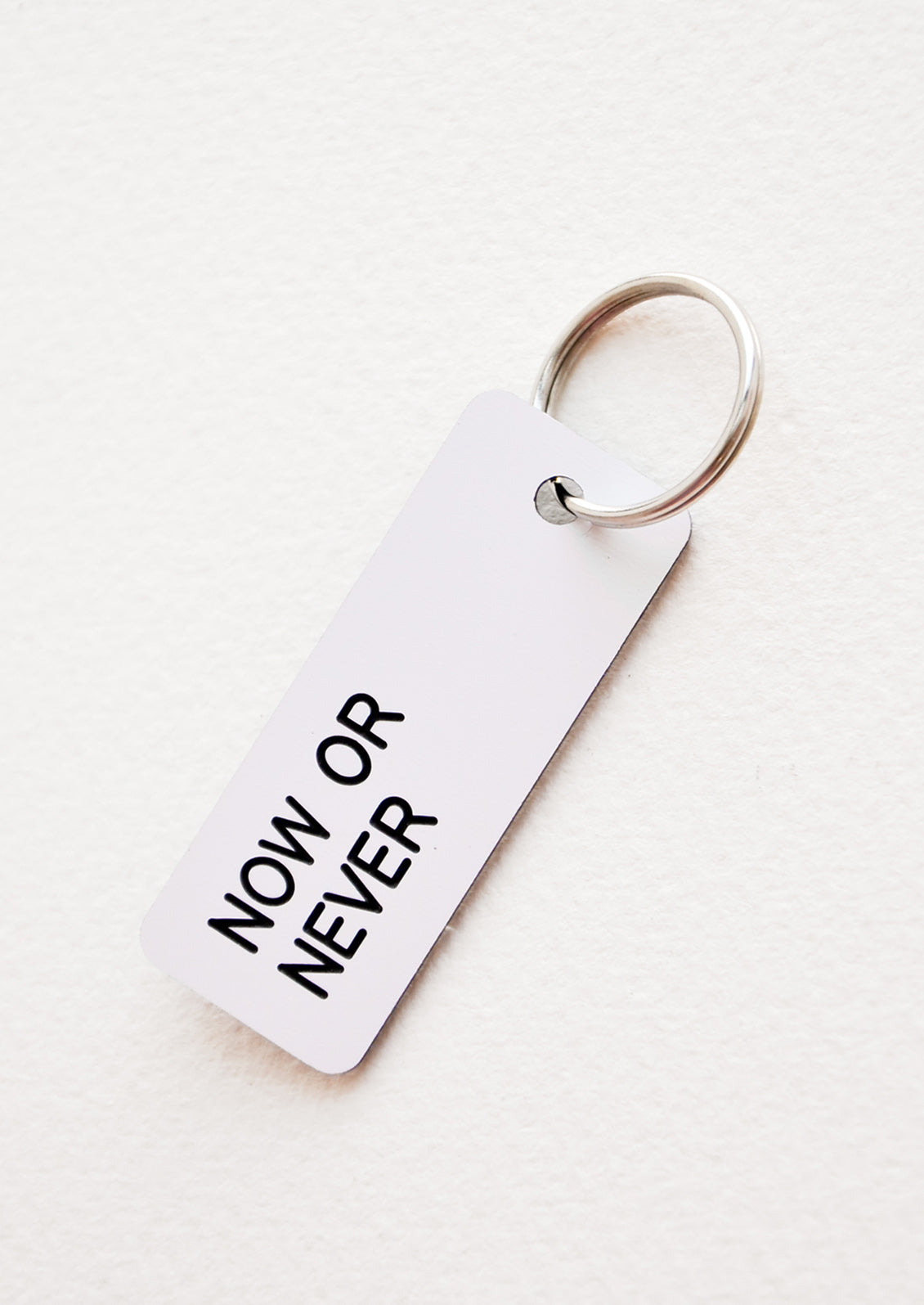 Small acrylic keychain, white background with black words that says "NOW OR NEVER"