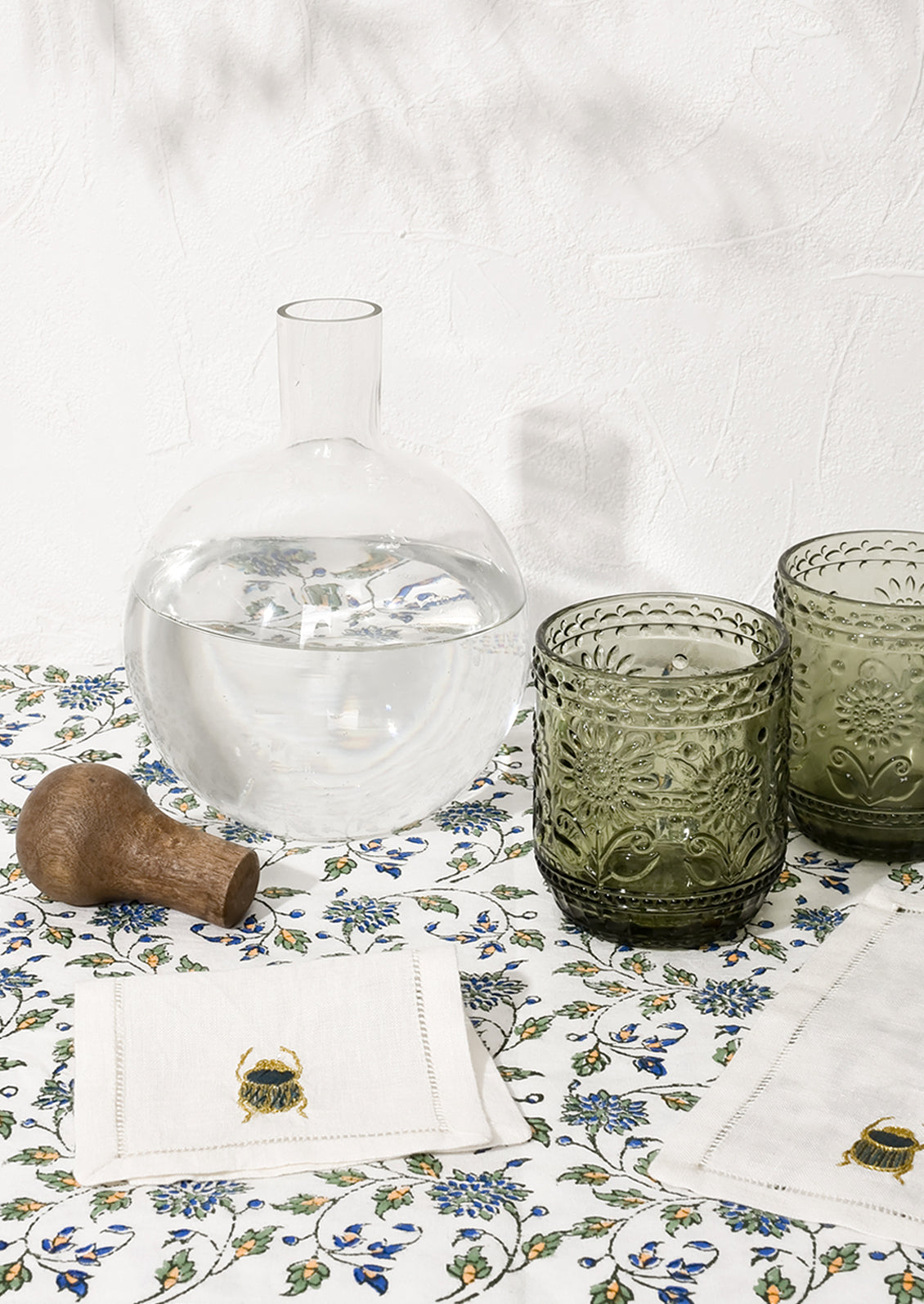 A glass decanter shown with green glasses and cocktail napkins.