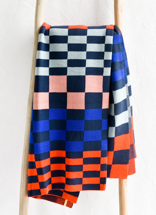 A knit throw blanket in checker print pattern in navy, light blue, royal blue, pink and orange.