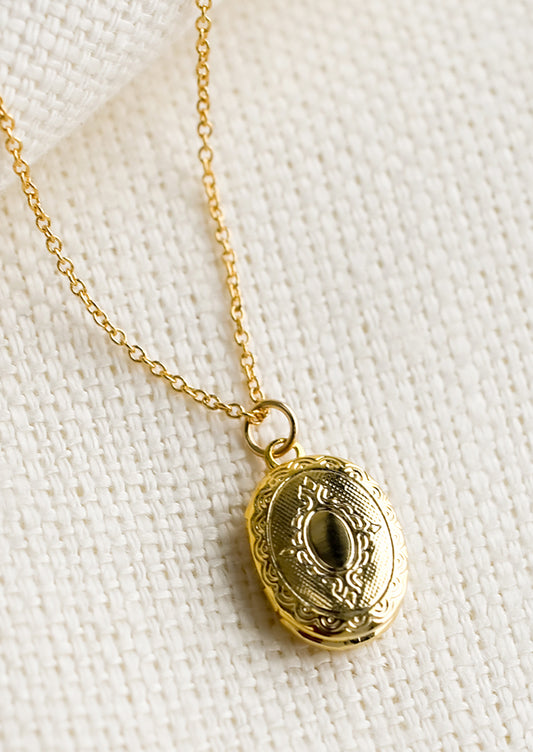 A oval shaped locket necklace with antique inspired engraving.