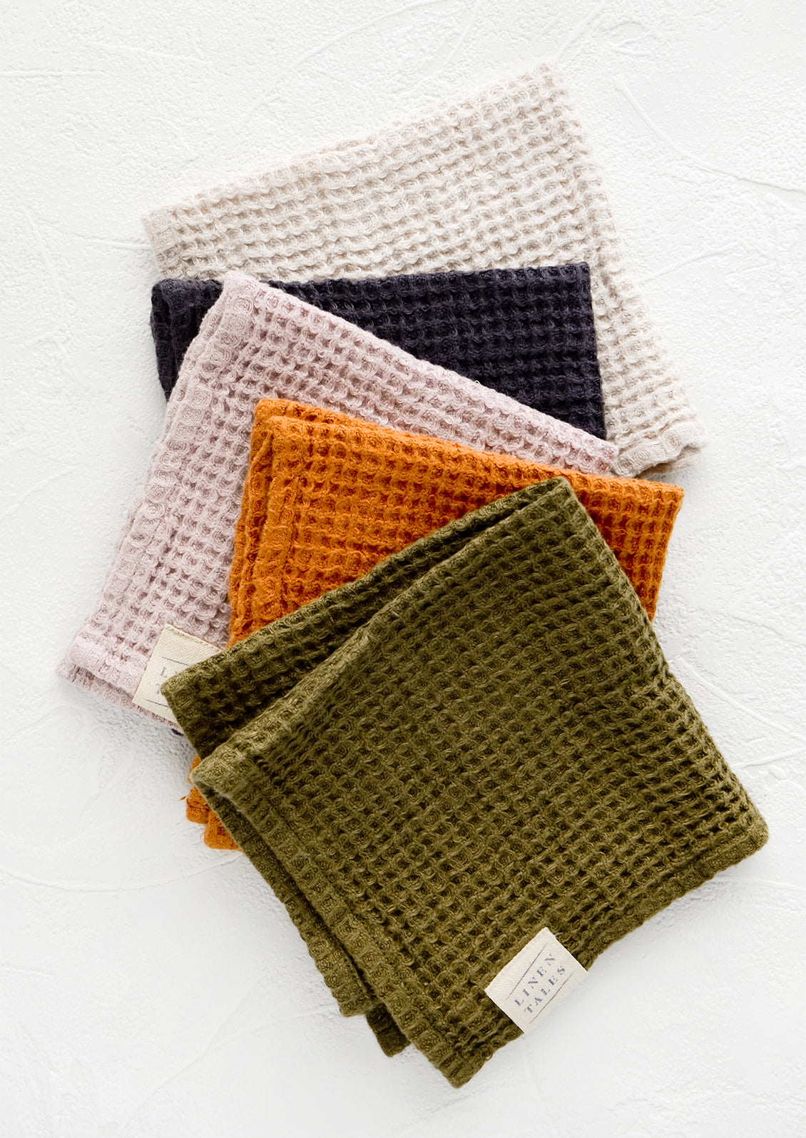 A row of folded waffle-weave linen washcloths, in an assortment of color options.