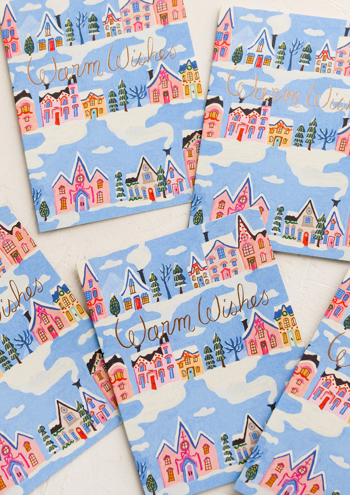 Greeting card with blue background and repeating rows of houses and trees. "Warm Wishes" written in copper script.