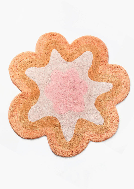 A wavy edge flower shaped bath mat in peach and pink.