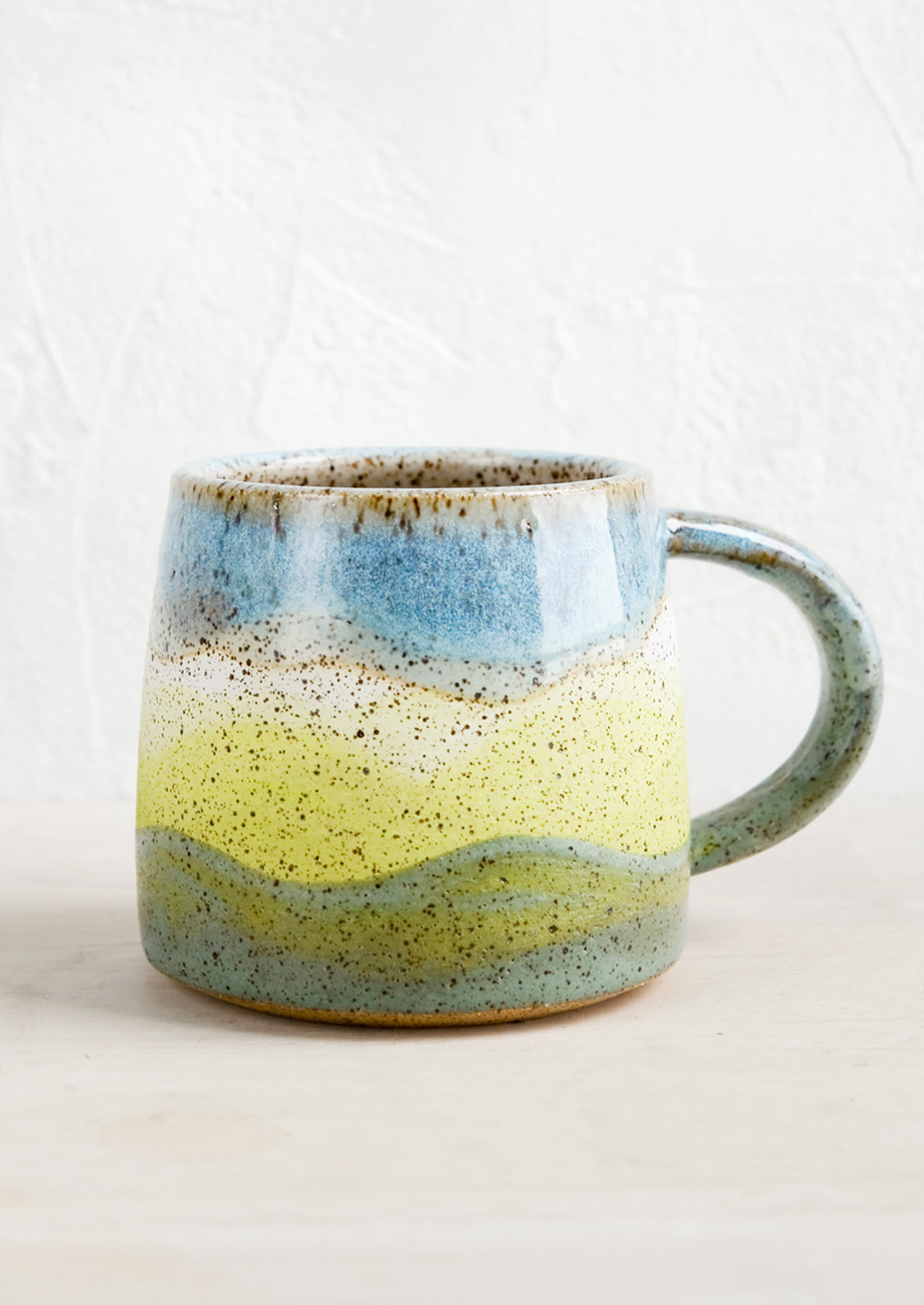 A ceramic mug with handle in wavy stripe design in celadon, lime and blue.