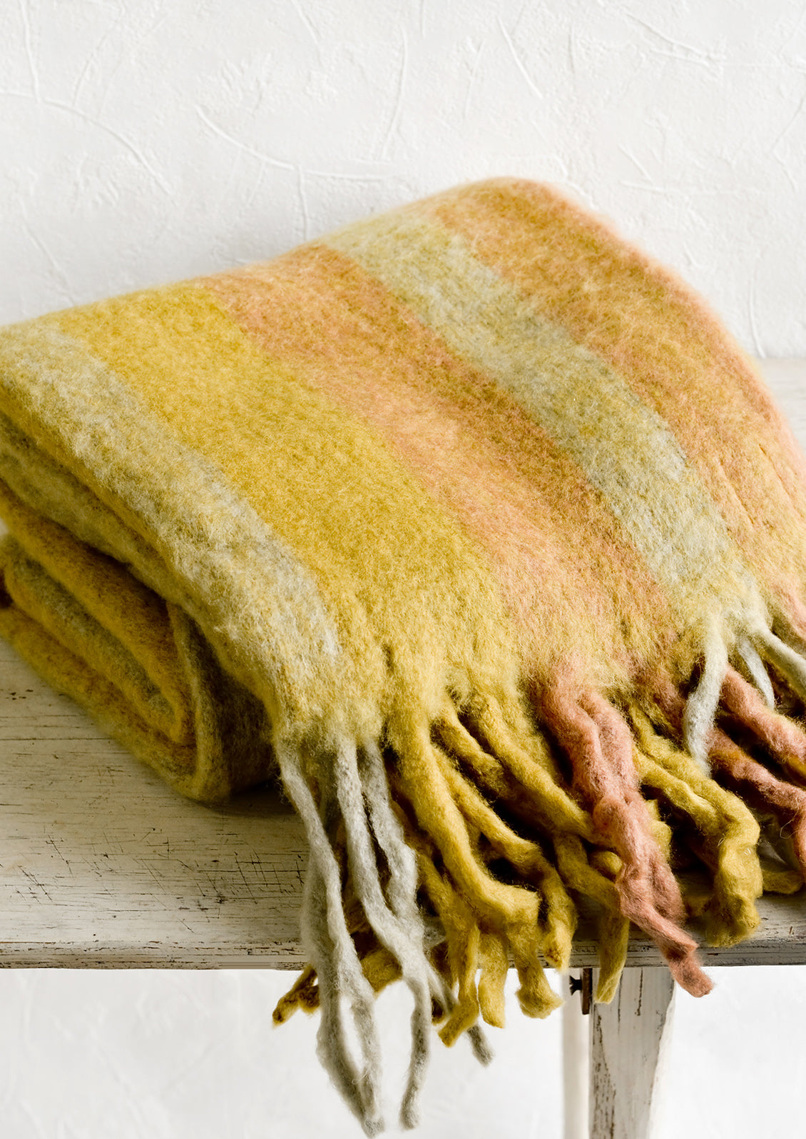 A fuzzy throw blanket with exaggerated fringe in wheat multi.