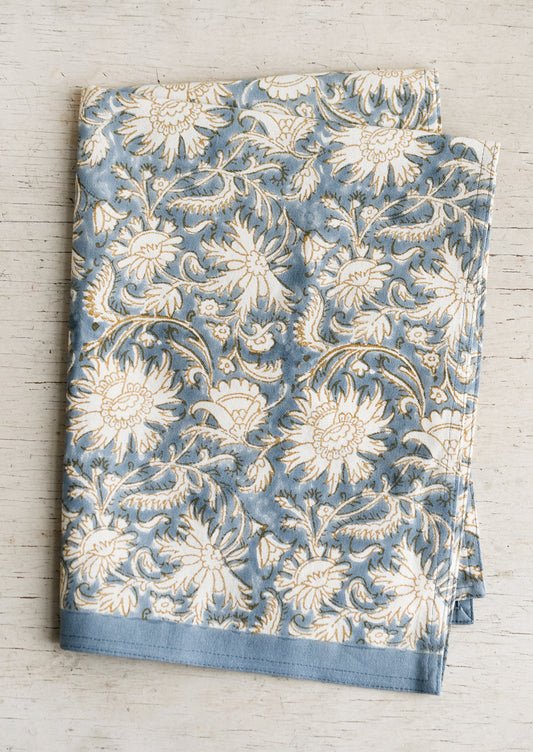 A block printed tea towel with floral pattern in blue, white and tan.