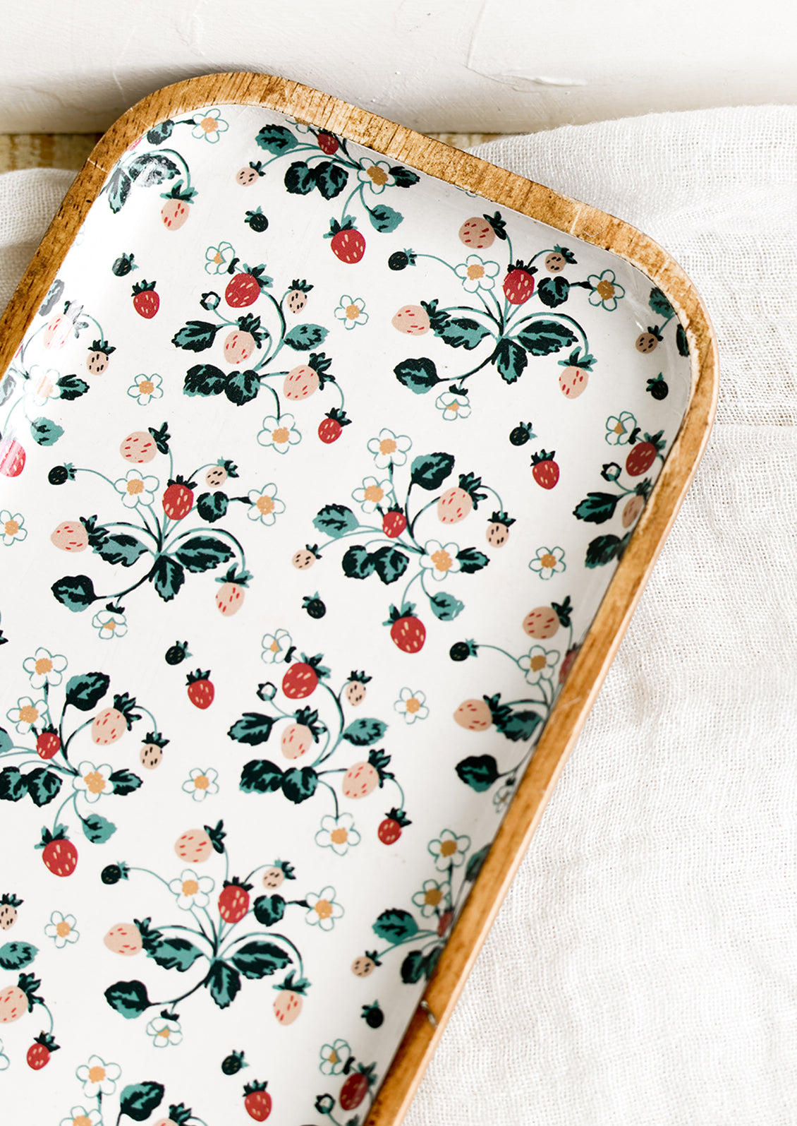 A rectangular wooden tray with white strawberry enamel pattern.