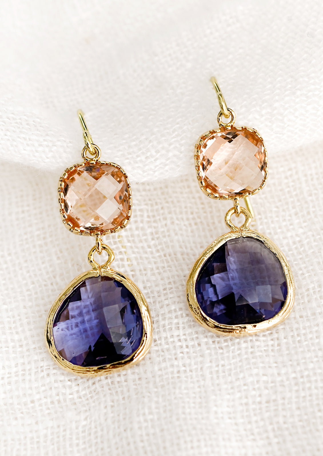 A pair of two-stone bezeled gem earrings in peach and tanzanite.