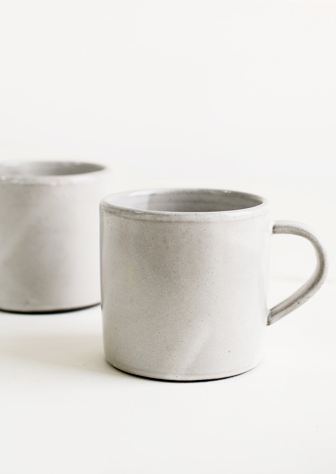 Two identical ceramic coffee mugs in a simple, classic shape in a white glaze over brown clay.