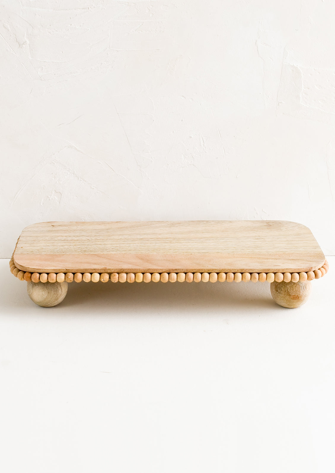 A rectangular wooden riser with round feet and beaded detail.