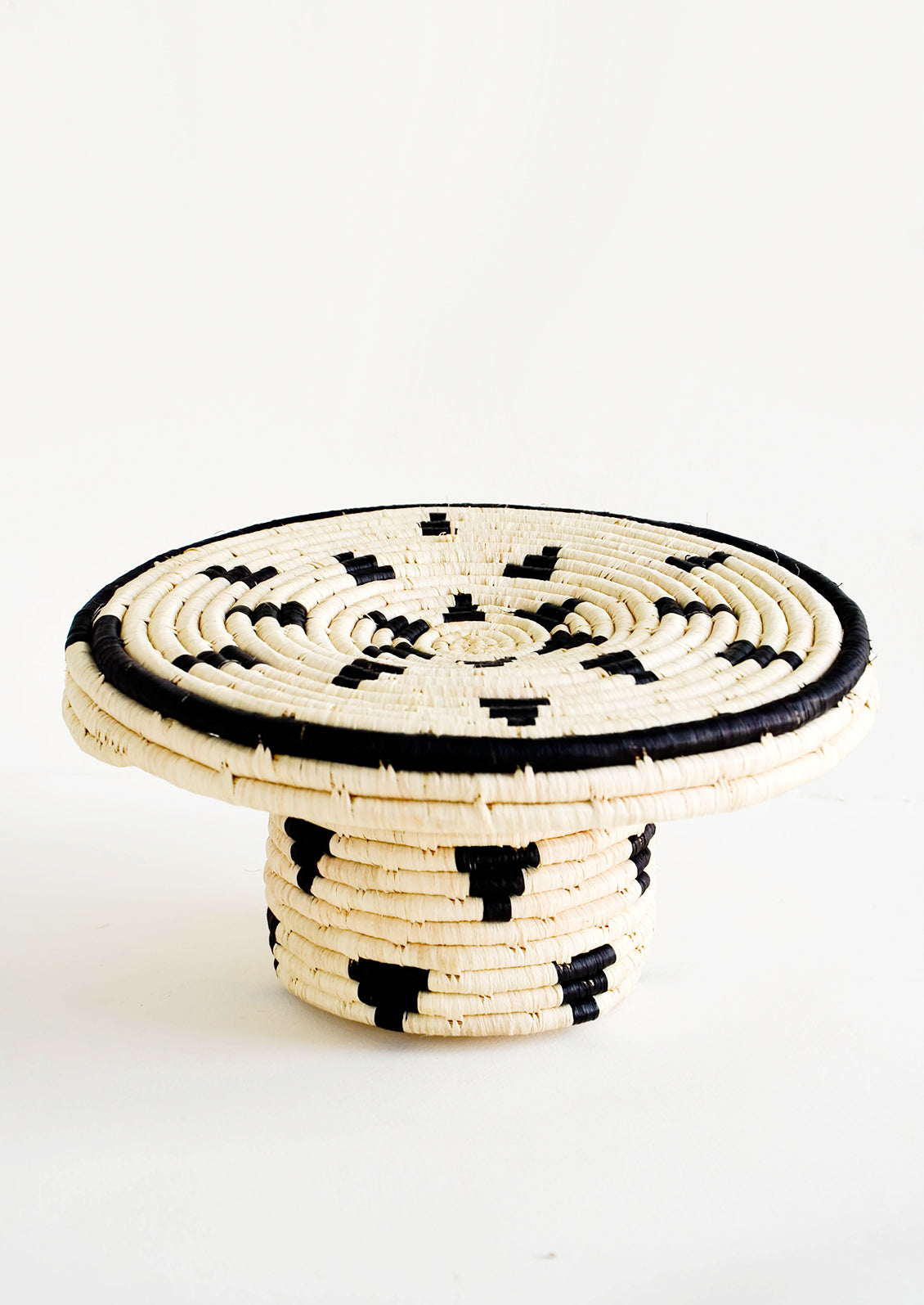 Round woven raffia cake stand in natural with black triangle print