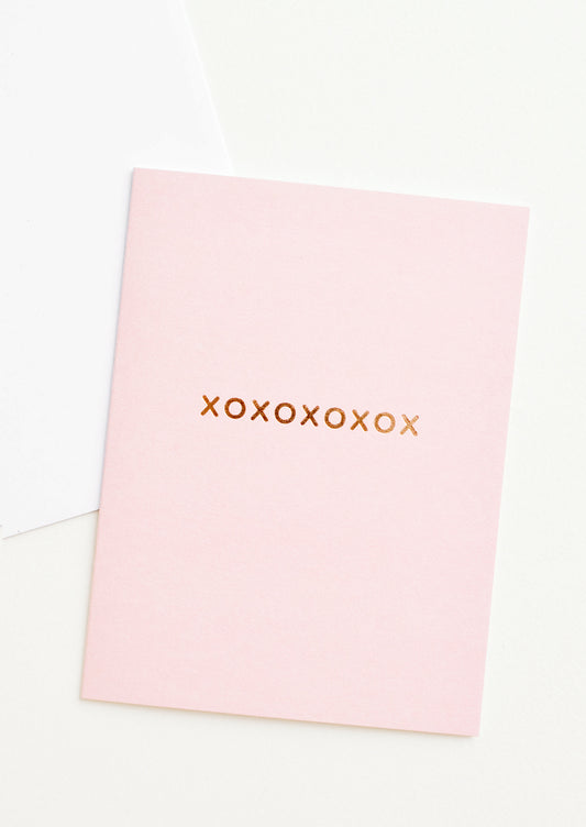 A pale pink greeting card with "xoxoxoxoxox" in gold foil.