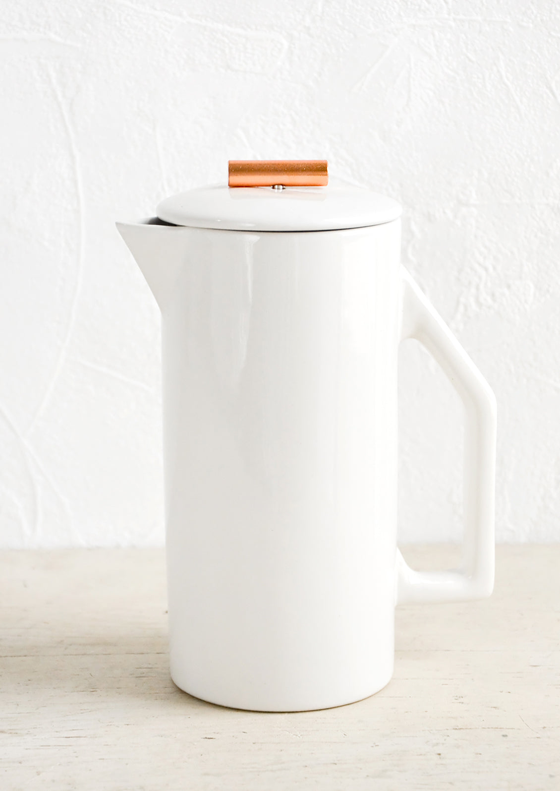 A french press coffee maker made from white ceramic with a copper rod on lid.