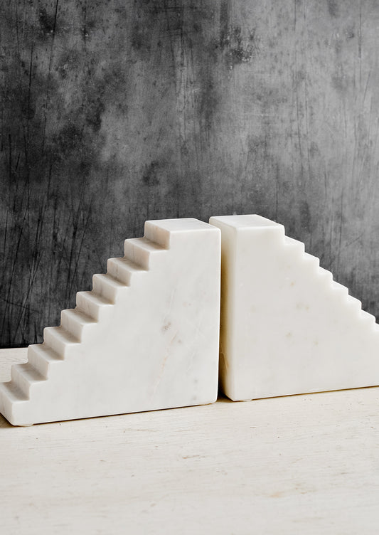 A pair of white marble bookends with staircase design.