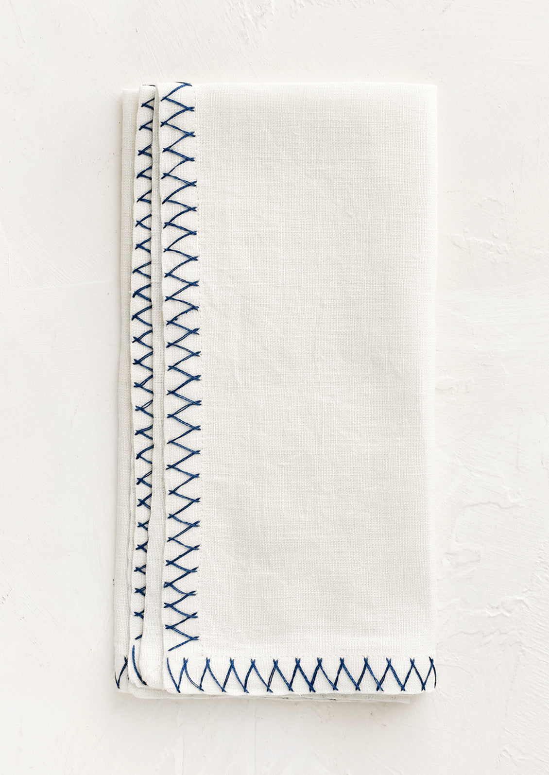 A white linen napkin with blue embroidered zig zag border.