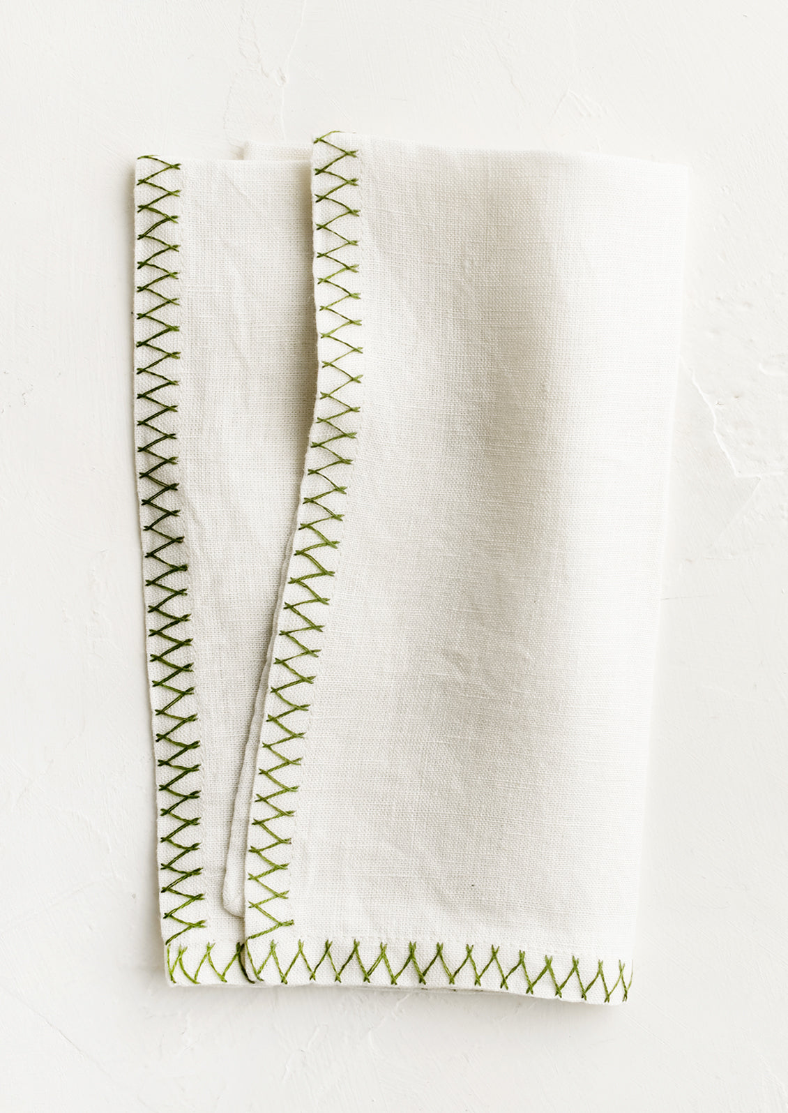 A white linen napkin with green embroidered zig zag border.