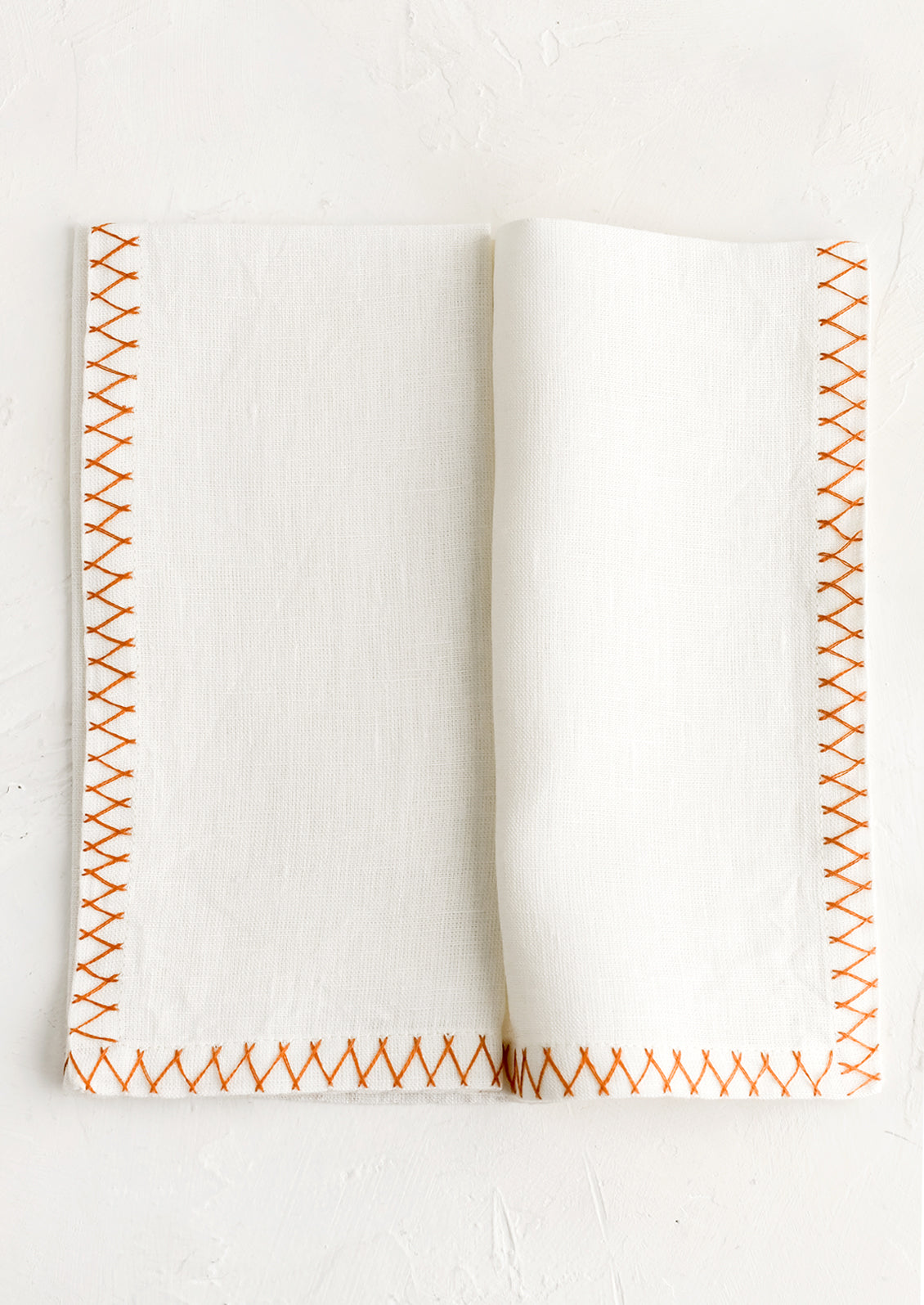 A white linen napkin with orange embroidered zig zag border.