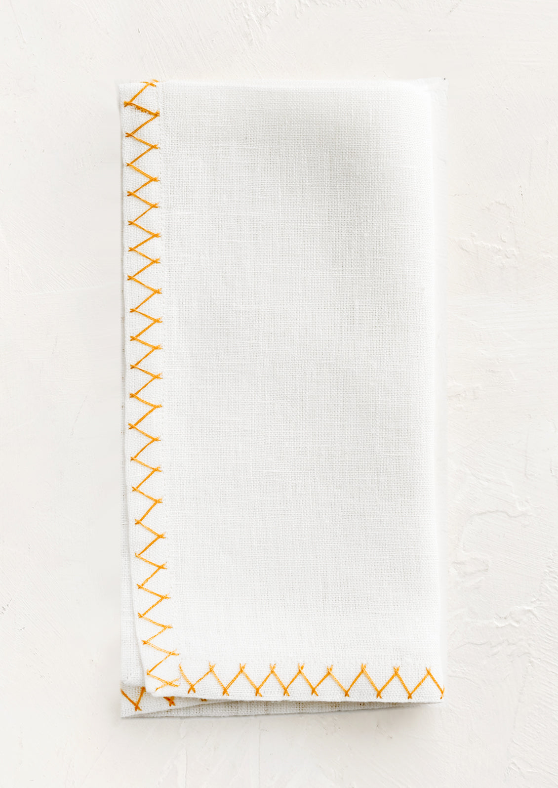 A white linen napkin with yellow embroidered zig zag border.